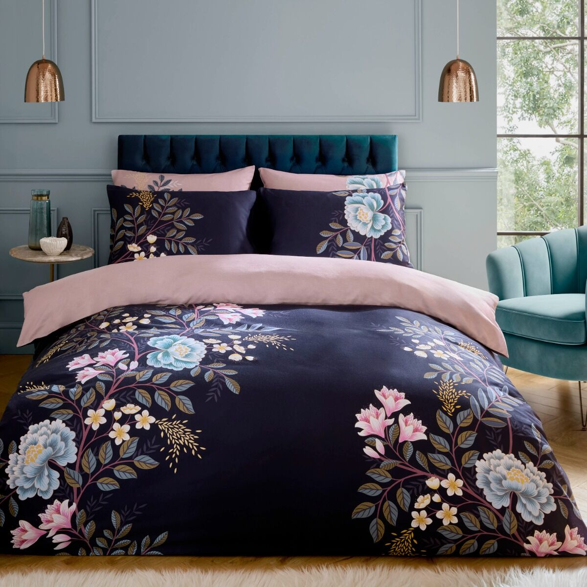 Floral bedding set on a bed in a stylish bedroom with a teal chair and gray walls.
