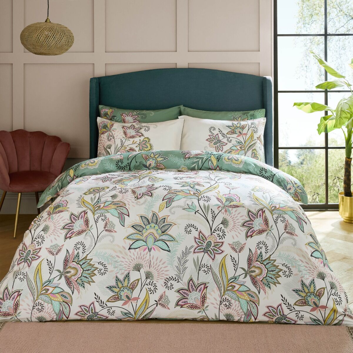 Floral bedding set on a bed with a green headboard in a room with a window and plant.