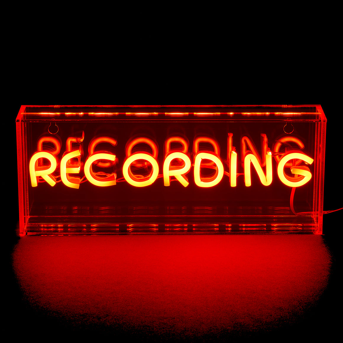 Neon sign with 'RECORDING' text inside a red cassette tape-shaped frame on a black background.