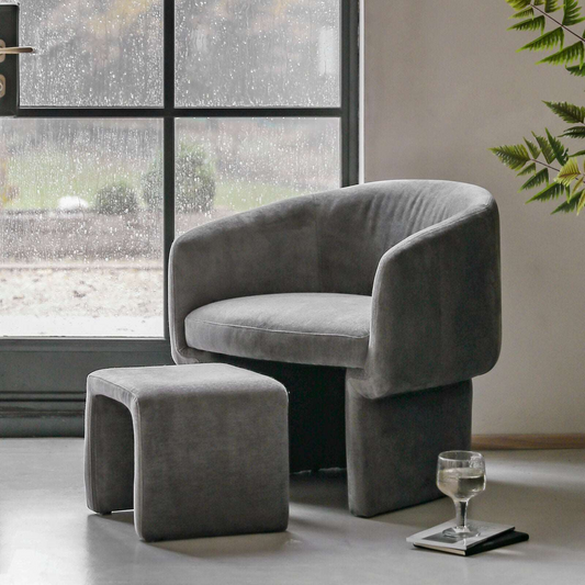 Gray armchair with matching ottoman in a room with large windows and a plant.