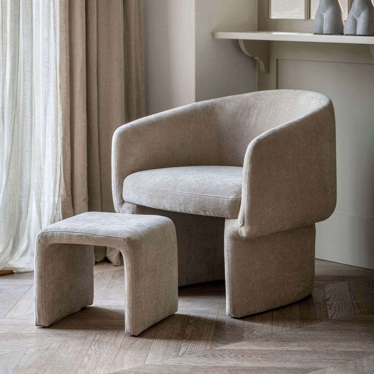 Beige armchair and ottoman in a room with curtains and a shelf.