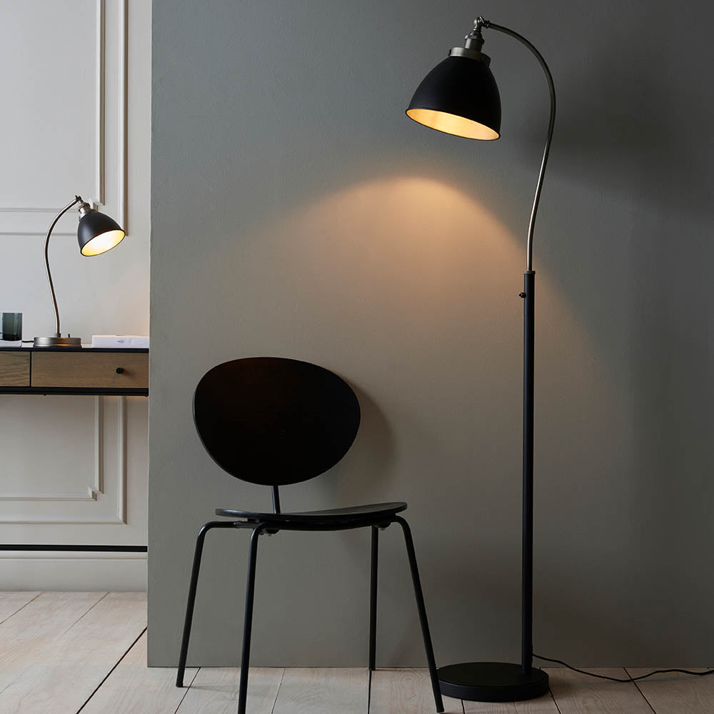 Modern black floor lamp casting light on a chair in a minimalistic room.