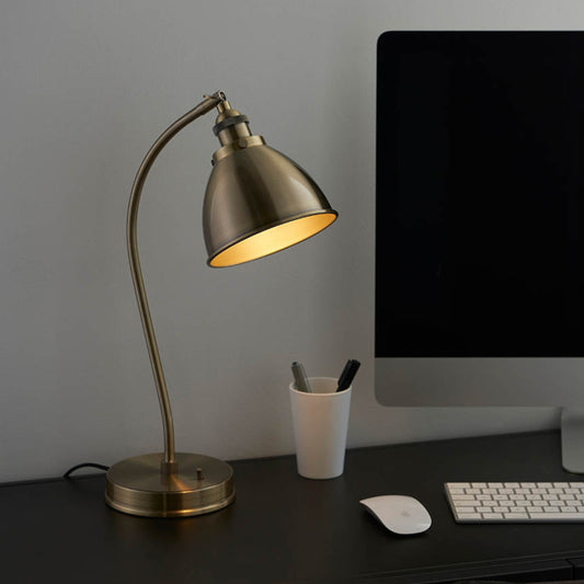Brass desk lamp on a dark desk with a computer monitor and keyboard.