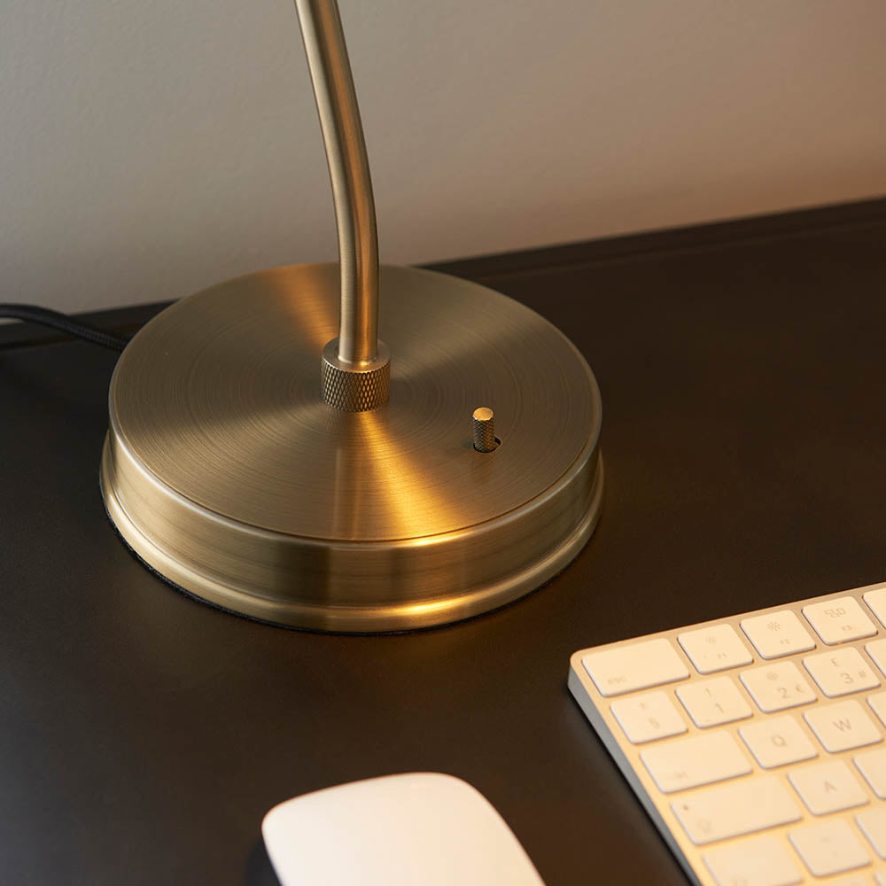 Gold desk lamp on a dark surface with a keyboard and mouse.