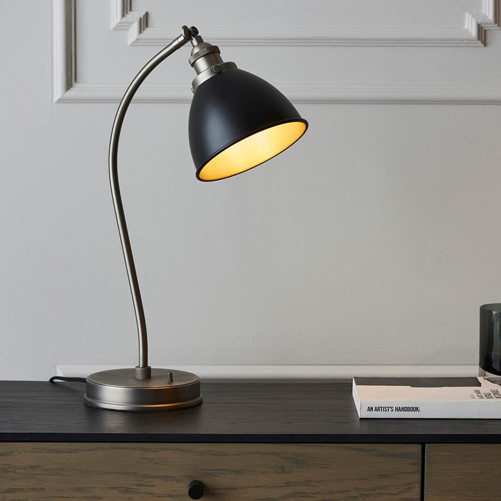 Table lamp with black shade and gold interior on a wooden surface.