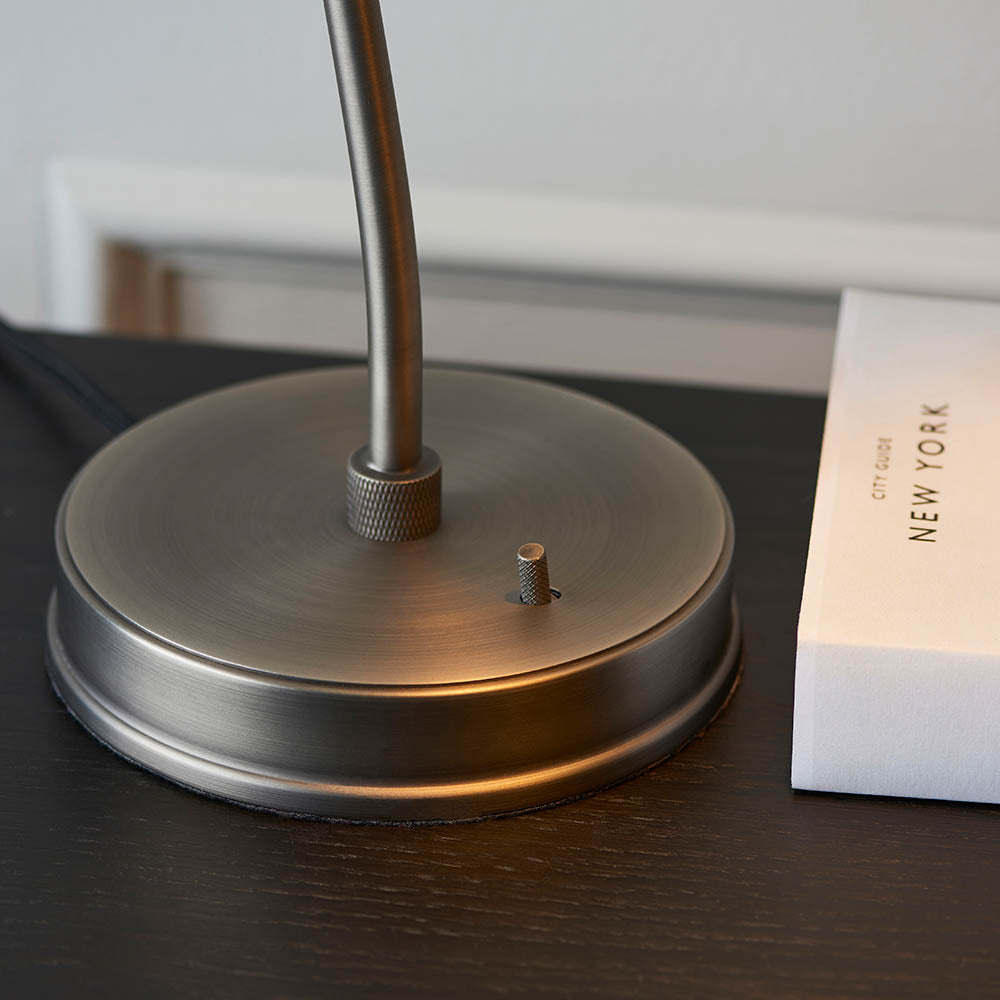 Metallic lamp base on a dark surface with a blurred book in the background
