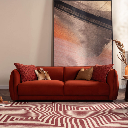Red sofa with decorative pillows in a living room setting with abstract art on the wall.