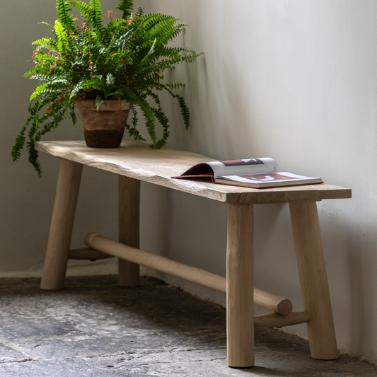 Wooden bench with a plant and books on a stone floor against a white wall
