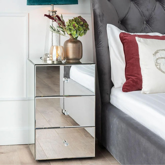 Mirrored nightstand with decorative items next to a bed with pillows.