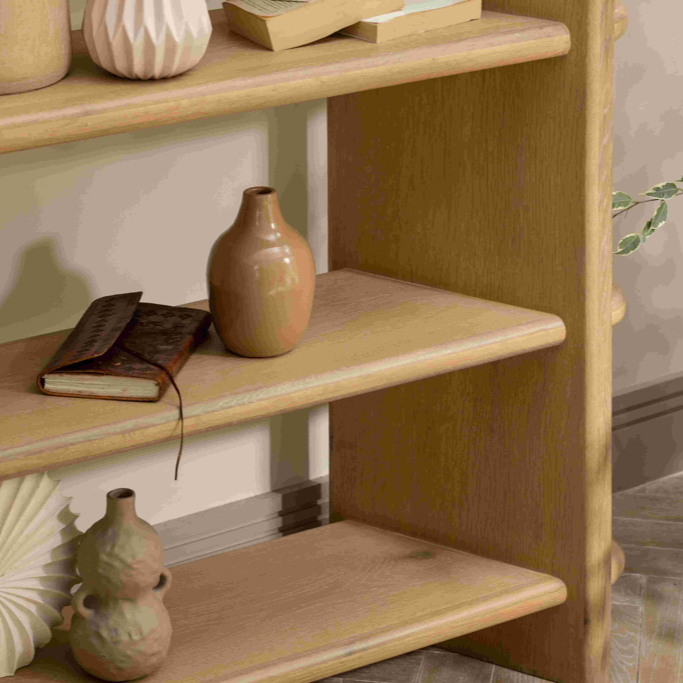 Wooden shelf with decorative vases and a book against a neutral wall.
