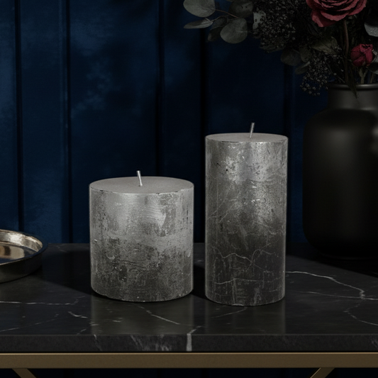 Two gray candles on a dark surface with a dark blue wall in the background.
