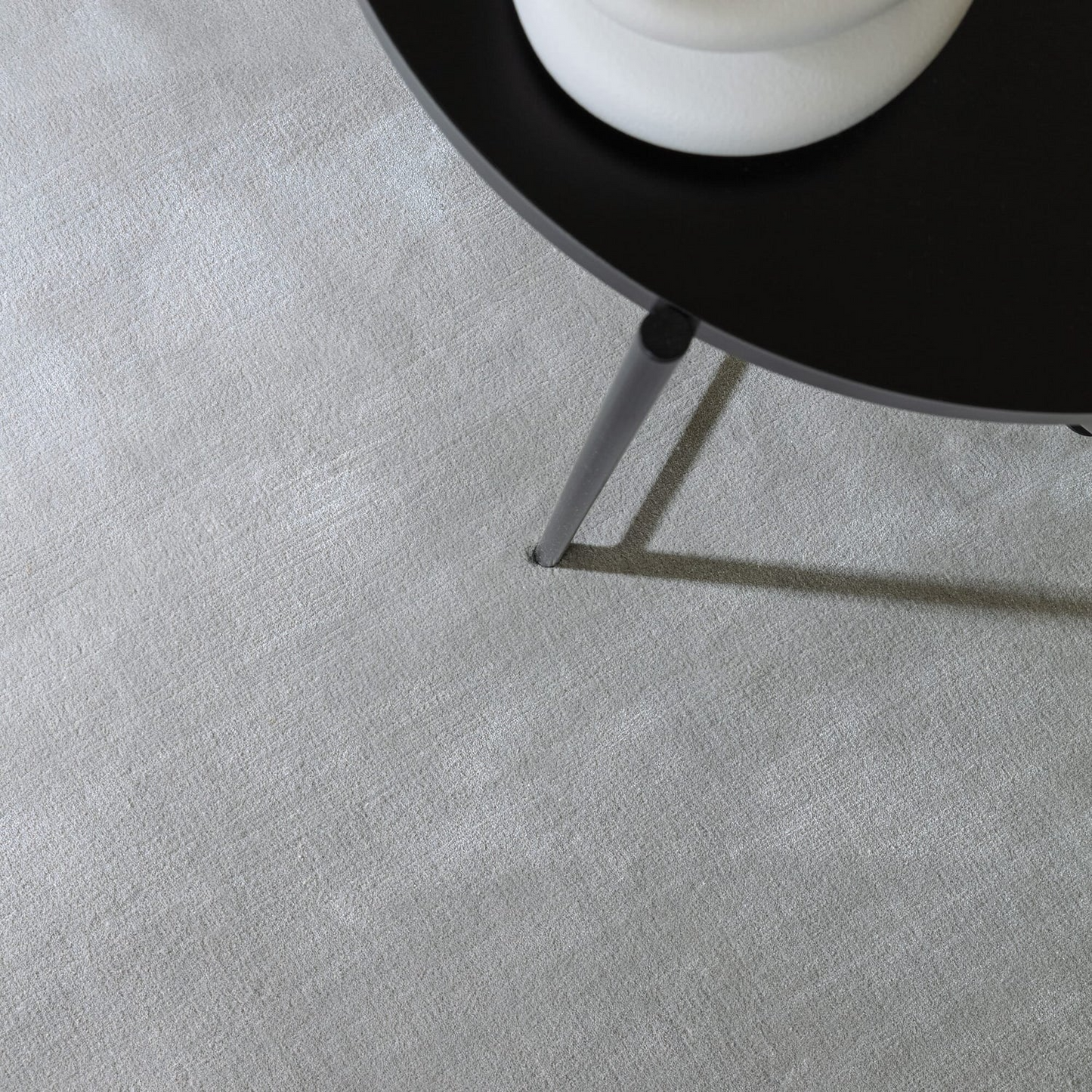 Close-up of a black chair leg on a textured gray rug