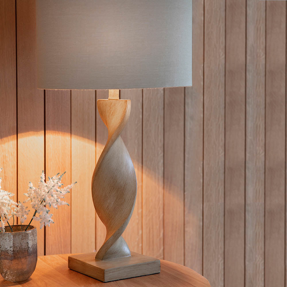 Wooden table lamp with a gray shade on a wooden surface against a wooden wall.