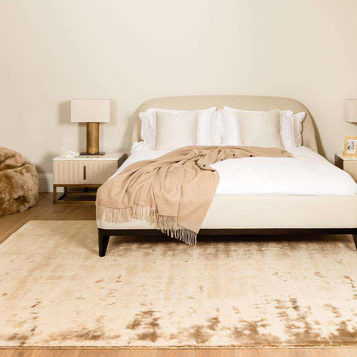 Neatly made bed with beige blanket and pillows in a bedroom setting.