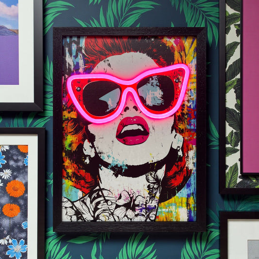 Framed artwork with a colorful design of a face wearing pink sunglasses on a patterned wall.