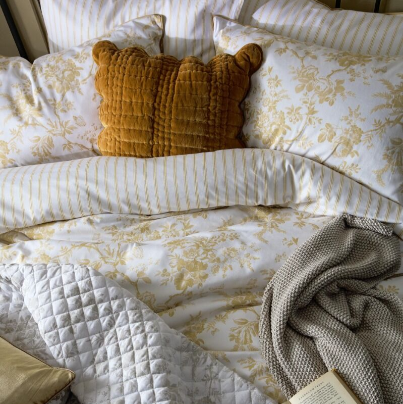 Cozy bedroom scene with floral bedding, pillows, and a book.