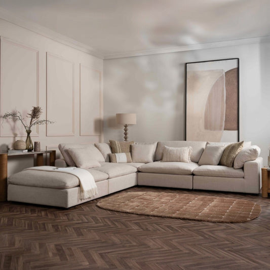 Modern living room with a beige sectional sofa, abstract art, and wooden floor.