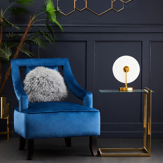 Blue armchair with a fluffy cushion in a room with geometric wall art and a gold side table.