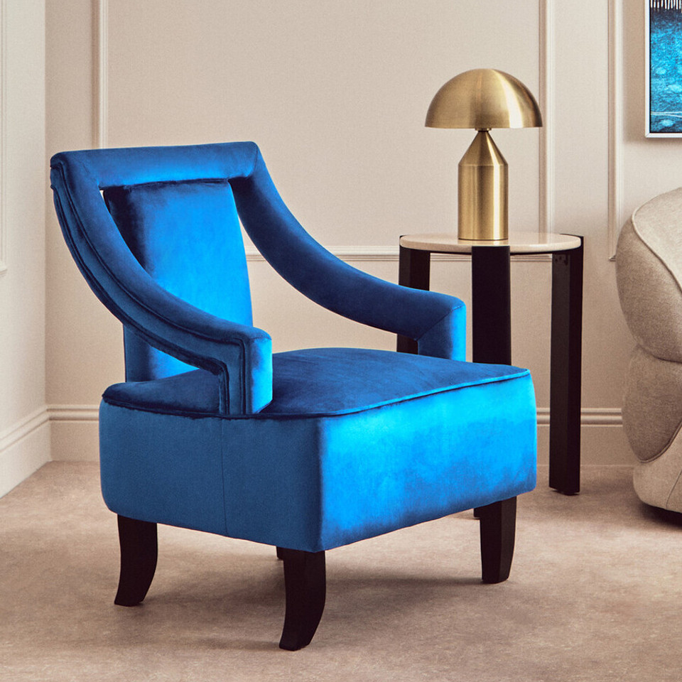 Blue armchair in a stylish room with a gold lamp and beige walls.