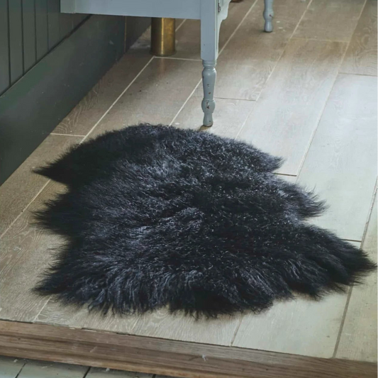 A black shaggy faux fur rug placed on a light wood plank floor in a bathroom setting, with a gray vanity cabinet visible in the background.