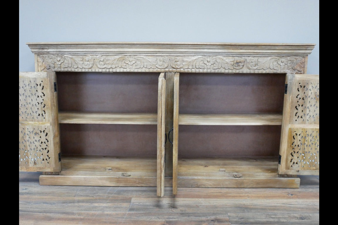 A large, hand-carved solid wood sideboard measuring 190cm wide by 101cm high, featuring four intricately detailed doors with metal handles. The natural rustic finish highlights the ornate floral and geometric carvings, adding a touch of artisanal craftsmanship. Behind the doors are two spacious cupboards with internal shelves, offering ample storage. The wide counter-top provides additional surface space, making this piece both functional and decorative for various interior settings.