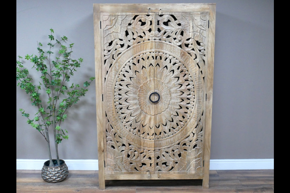 A tall, hand-carved solid wood wardrobe measuring approximately 109 in height, featuring intricate floral and geometric carvings on its doors. The natural wood finish highlights the craftsmanship, making it a statement piece suitable for various interior styles, including rustic, bohemian, and eclectic decor.