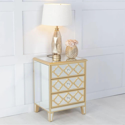 Decorative nightstand with mirror finish and gold accents, featuring a lamp and decorative items on top.