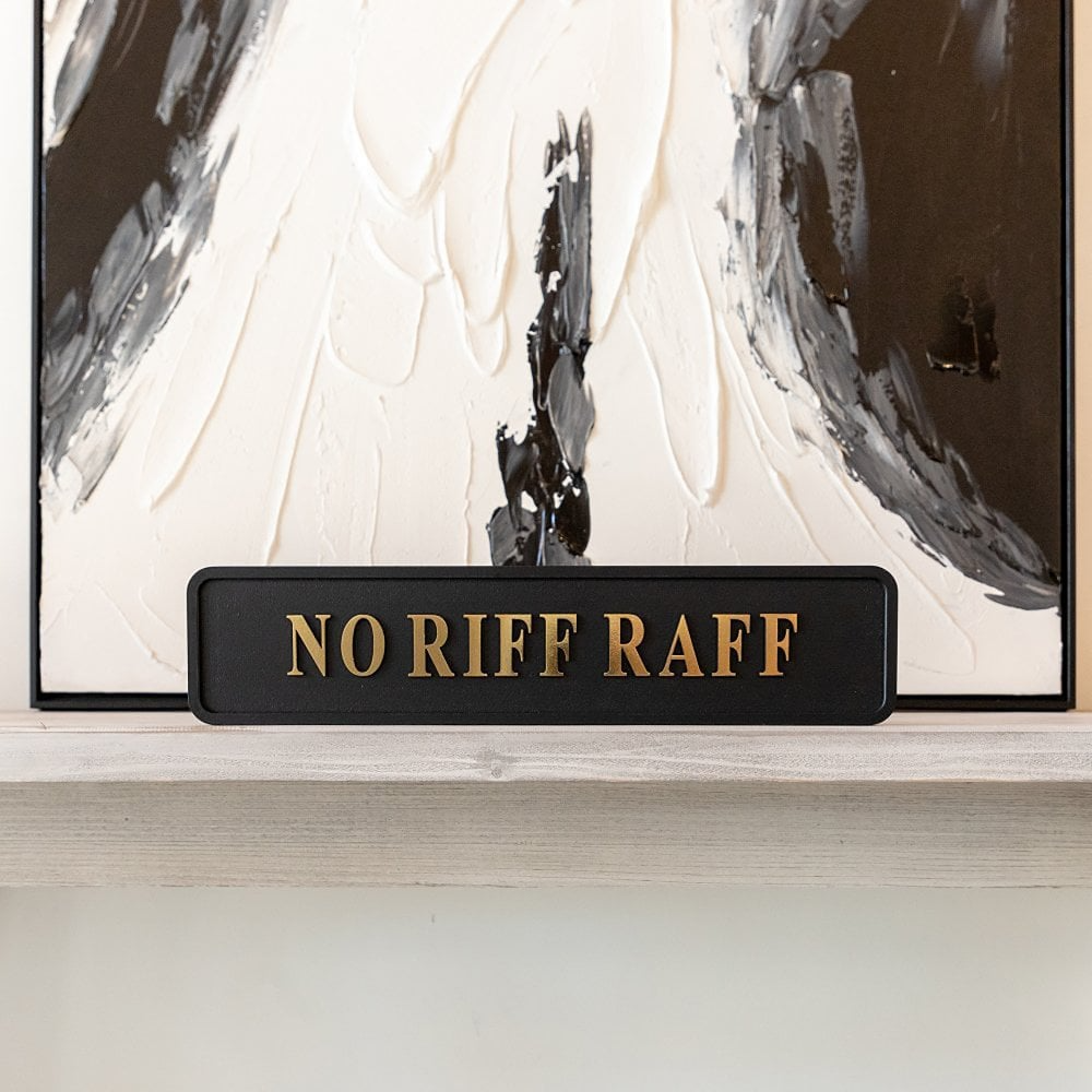 Decorative sign with 'NO RIFF RAFF' text in front of an abstract painting.