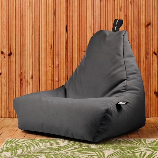 A dark gray bean bag chair with a zippered pocket, set against a vertical wood panel wall and a green tropical leaf pattern rug.