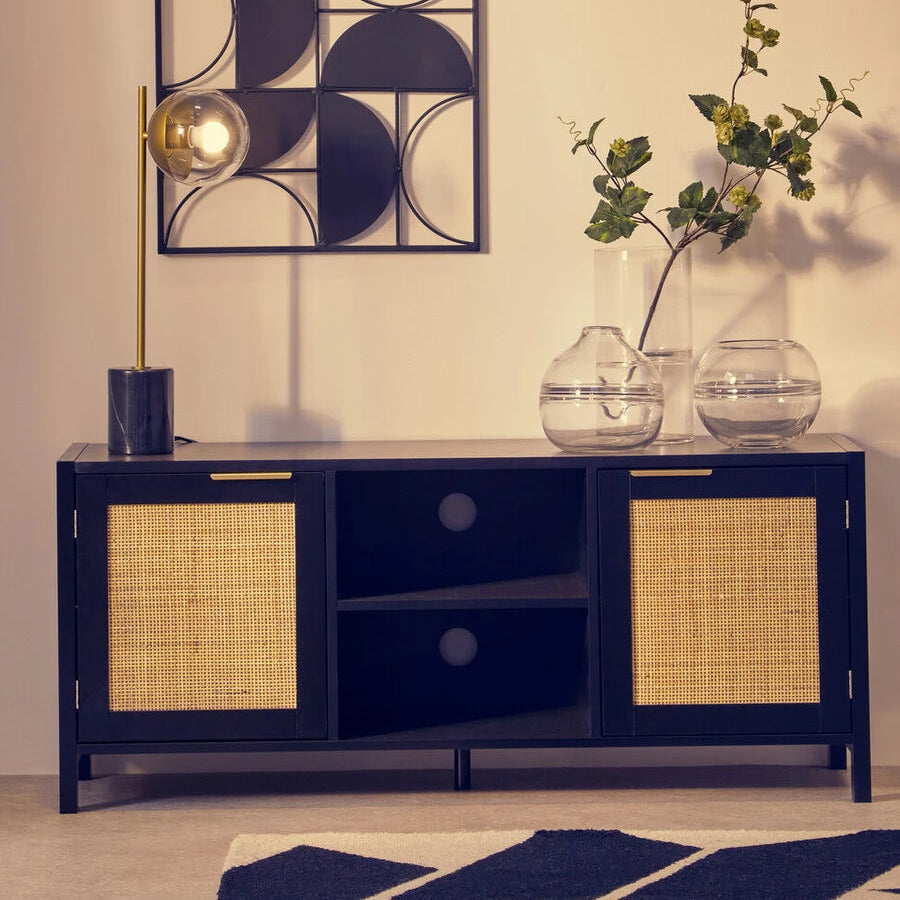 A modern black media unit with woven cane doors, styled in a minimalist room with a geometric wall art piece, a gold floor lamp, and glass vases.