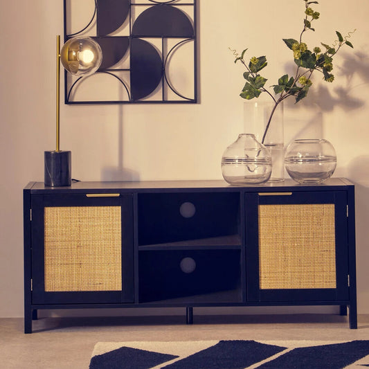 A modern black media unit with woven cane doors, styled in a minimalist room with a geometric wall art piece, a gold floor lamp, and glass vases.