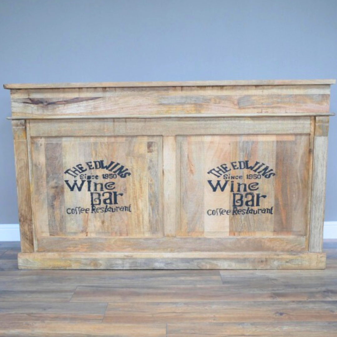 Elevate your entertaining space with this daring Rustic Mango Wood Bar Cabinet! Crafted from solid mango wood, its boho rustic charm is enhanced textured, natural details and bold black stamped accents that bring a unique edge. Featuring two spacious drawers, open shelves, and built-in wine racks, it offers generous storage to showcase your finest spirits and glassware. Ideal for rustic, boho, coastal interiors!