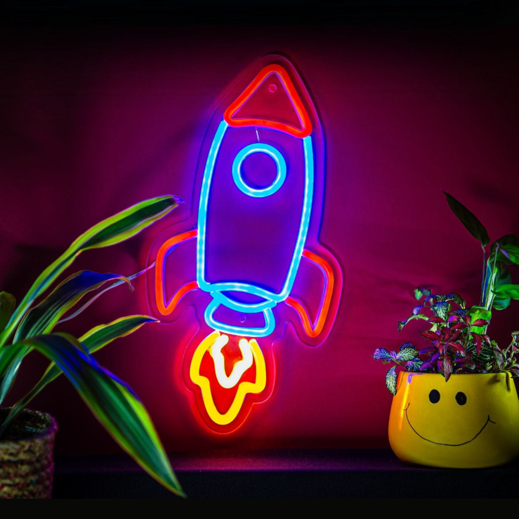 Neon sign of a rocket ship on a dark background with plants.
