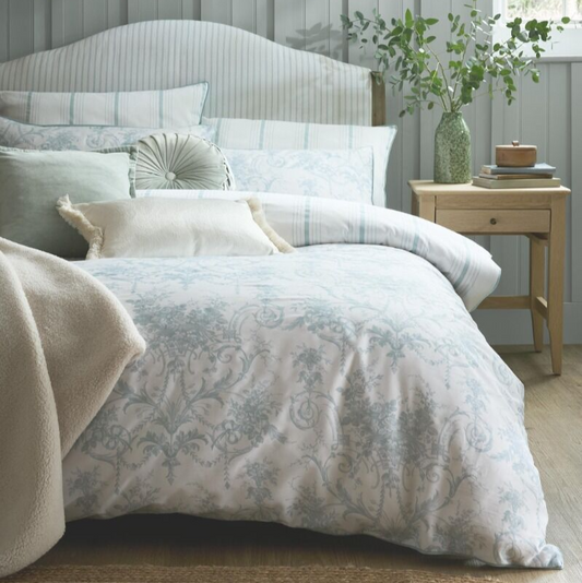 Bedroom with floral bedding, pillows, and a side table with a lamp and plant.