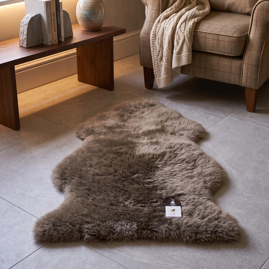 A natural brown sheepskin rug laid out on a light gray tiled floor in a cozy, modern living room setting with a wooden bench, armchair, and window.