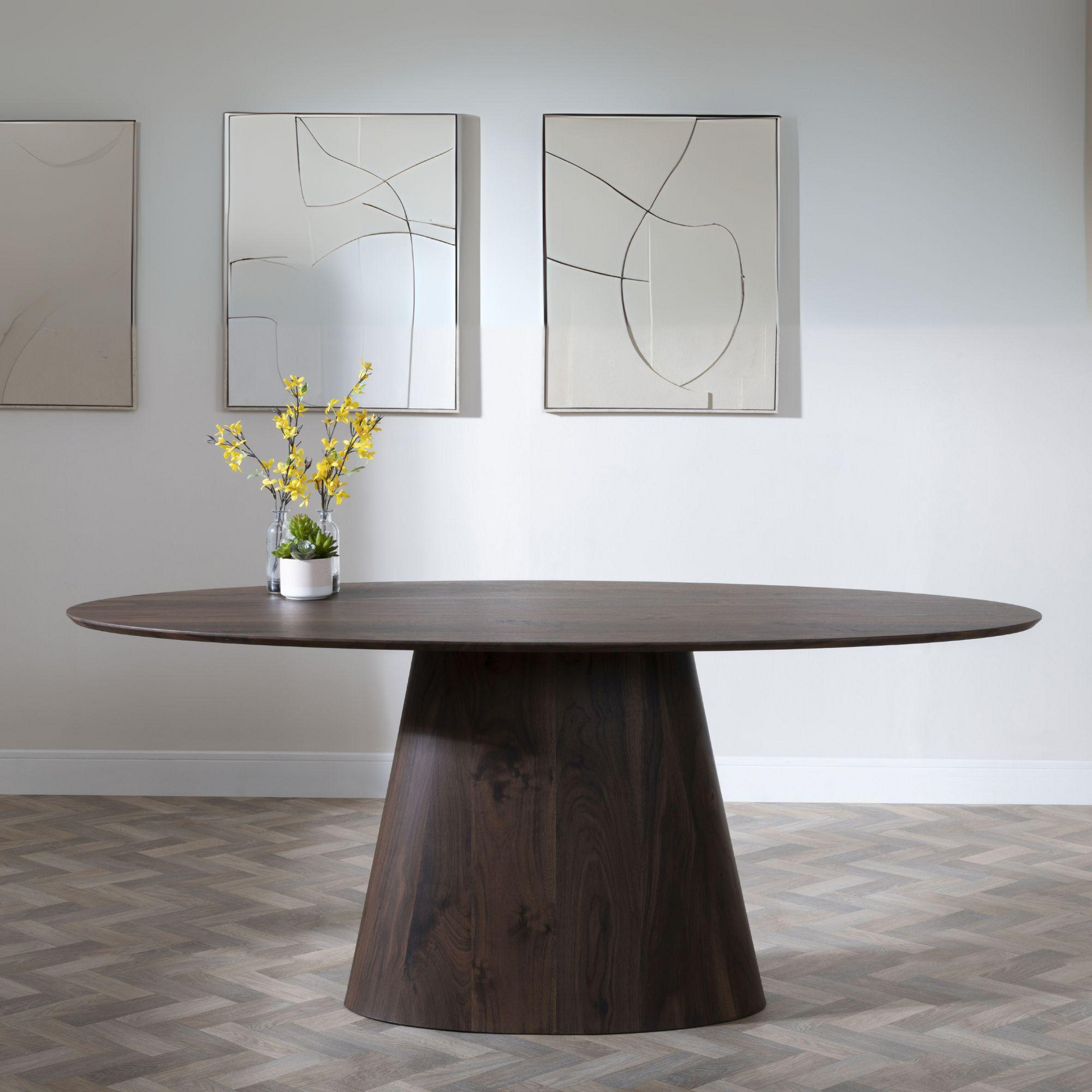 Wooden dining table with a vase of yellow flowers in a room with abstract art on the wall.
