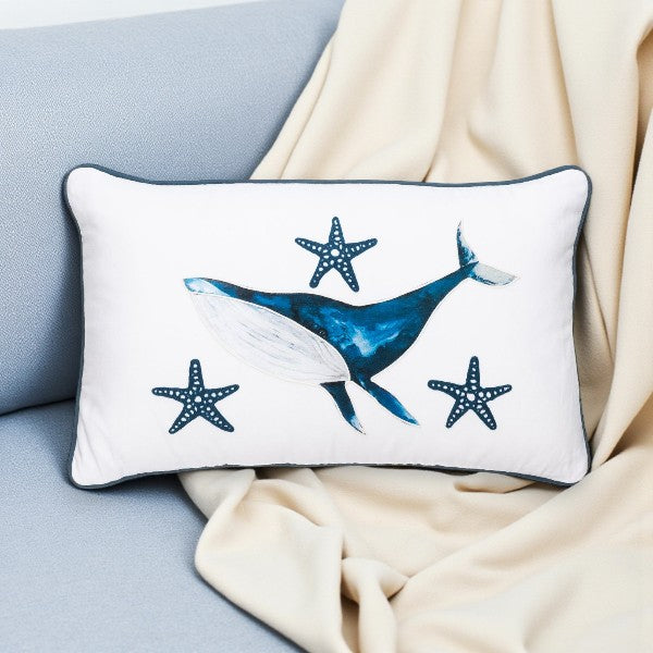Decorative pillow with whale and starfish design on a light blue couch.