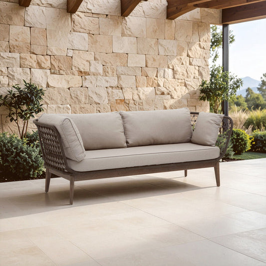 Outdoor sofa with beige cushions against a stone wall.