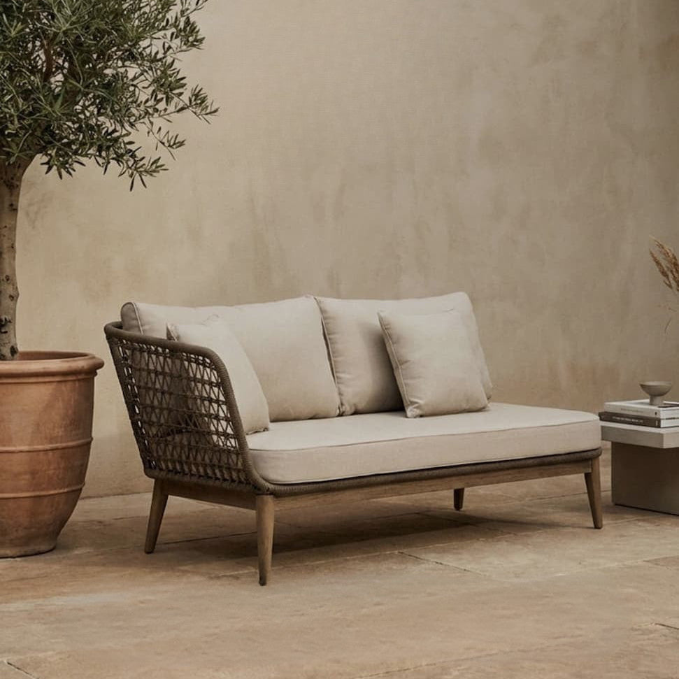 Outdoor seating area with a woven sofa and potted tree against a beige wall,