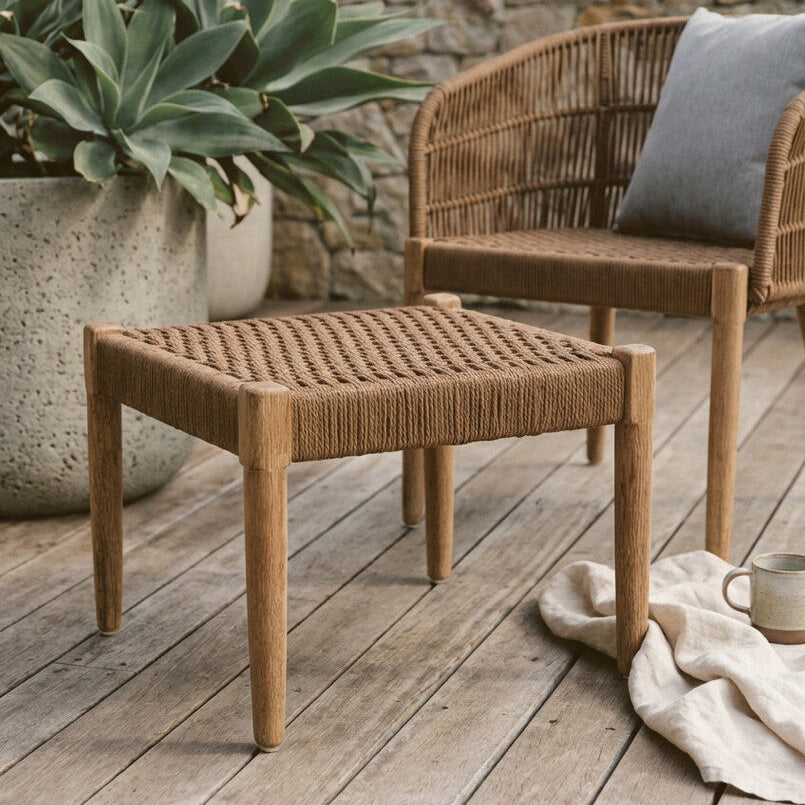 Wicker outdoor furniture set on a wooden deck with plants and a stone wall in the background.