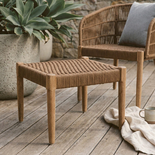 Wicker outdoor furniture set on a wooden deck with plants and a stone wall in the background.