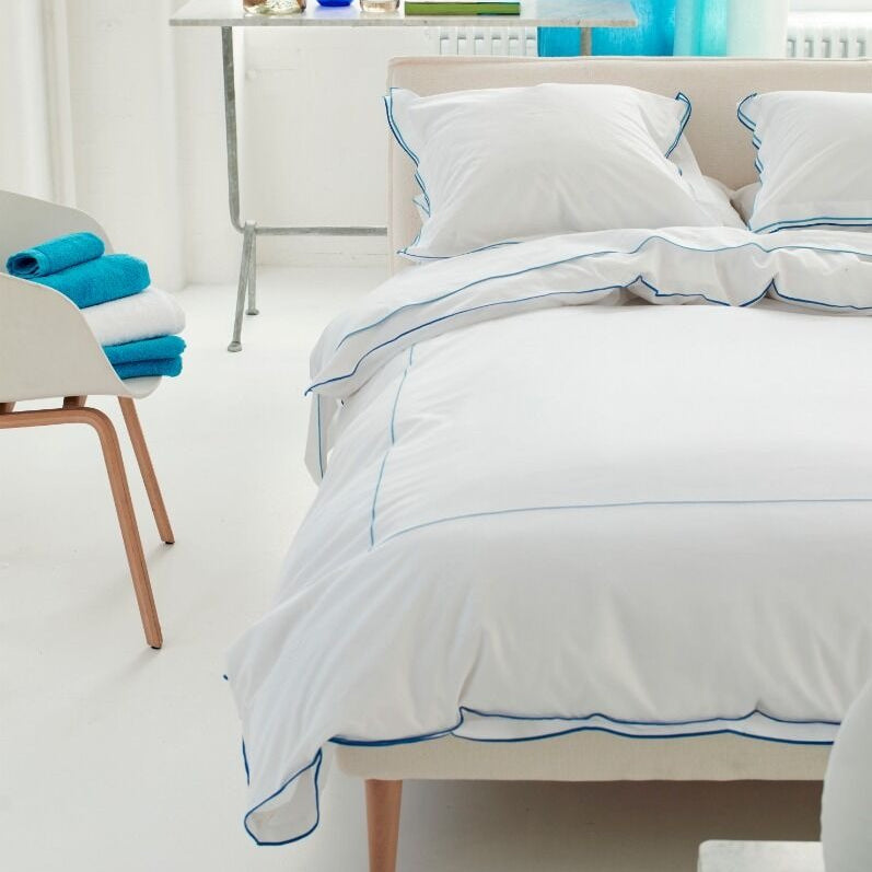 Bedroom with white bedding and blue accents, including a chair with blue towels and a window with blue curtains.
