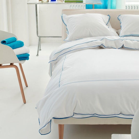 Bedroom with white bedding and blue accents, including a chair with blue towels and a window with blue curtains.