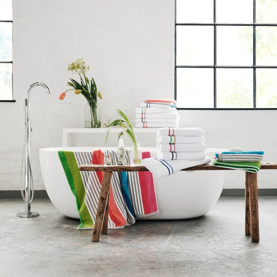 Modern bathroom with a freestanding bathtub, striped towels, and a wooden table.
