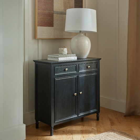 Black sideboard with a lamp and books against a neutral wall.