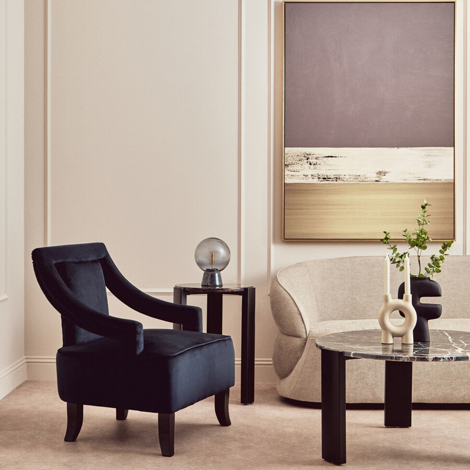 Modern living room with a black armchair, glass coffee table, and abstract painting.