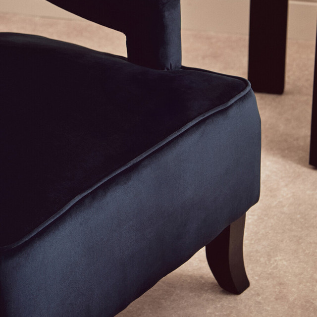 Close-up of a black velvet armchair on a beige carpet.