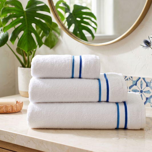 Stack of white towels with blue stripes on a bathroom counter, with a mirror and plant in the background.