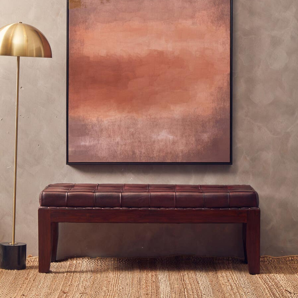 Abstract painting on a wall above a brown leather bench with a gold floor lamp to the left.