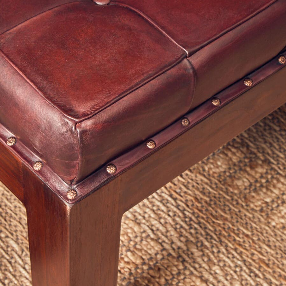 Close-up of a brown leather bench with wooden legs on a textured carpet.